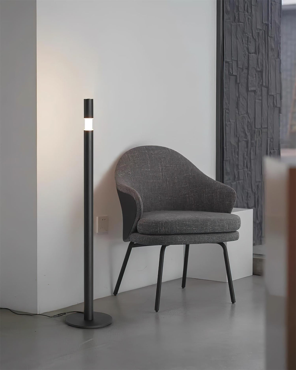 Lámpara de pie LED columna Tizona – negra junto a una butaca gris