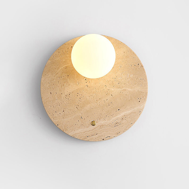 Aplique de pared de travertino con globo de cristal Pyria – sobre una pared blanca