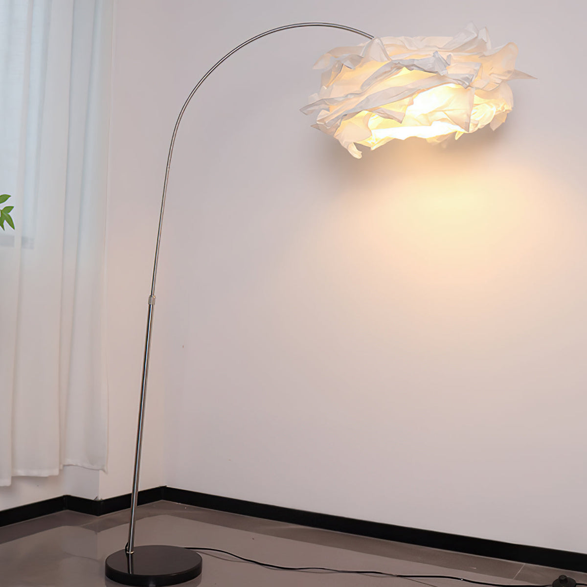 Lámpara de pie de arco con pantalla de papel Rizolva – encendida junto a una pared blanca