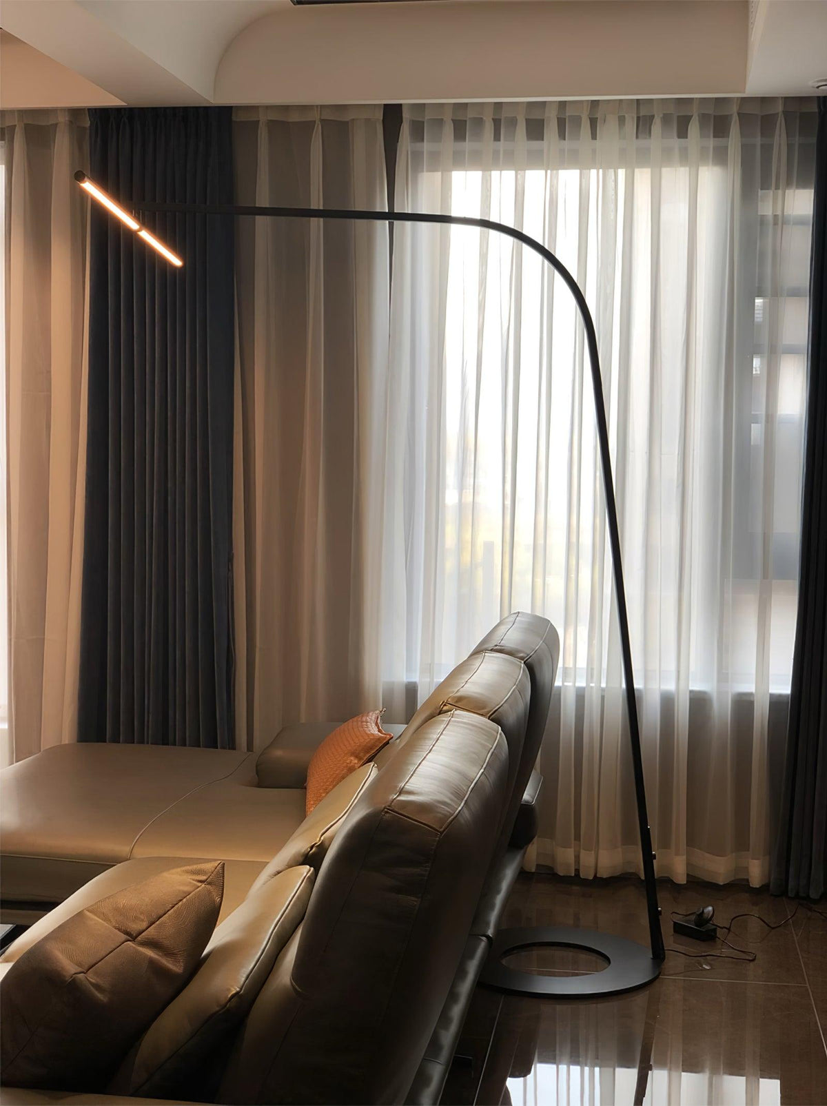 Lámpara de pie de arco LED Sigela – encendida junto a un sofá de piel
