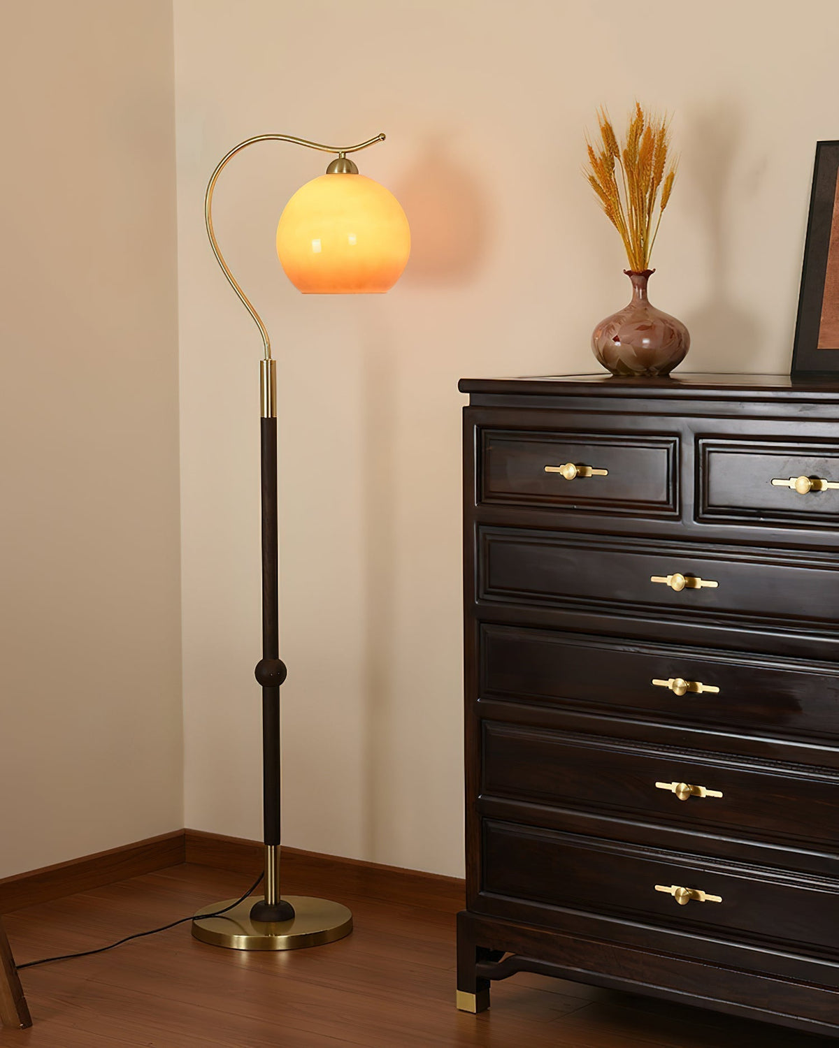 Lámpara de pie con globo de cristal Tostina – encendida junto a una cómoda de madera