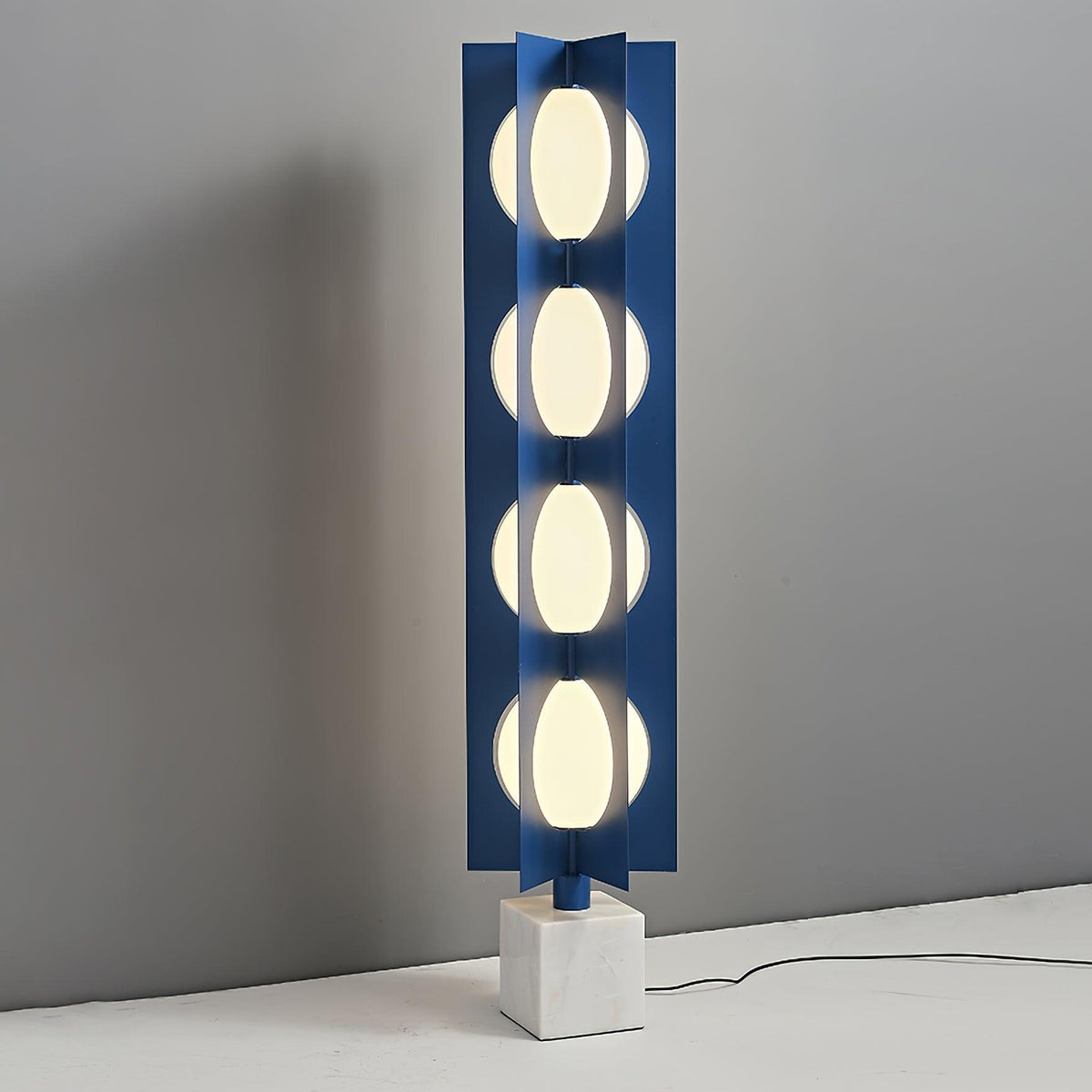 Lámpara de pie LED escultórica azul Toteva – encendida junto a una pared gris