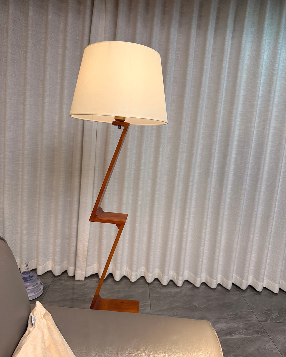 Lámpara de pie de madera en zigzag Zagora – junto a una cortina gris
