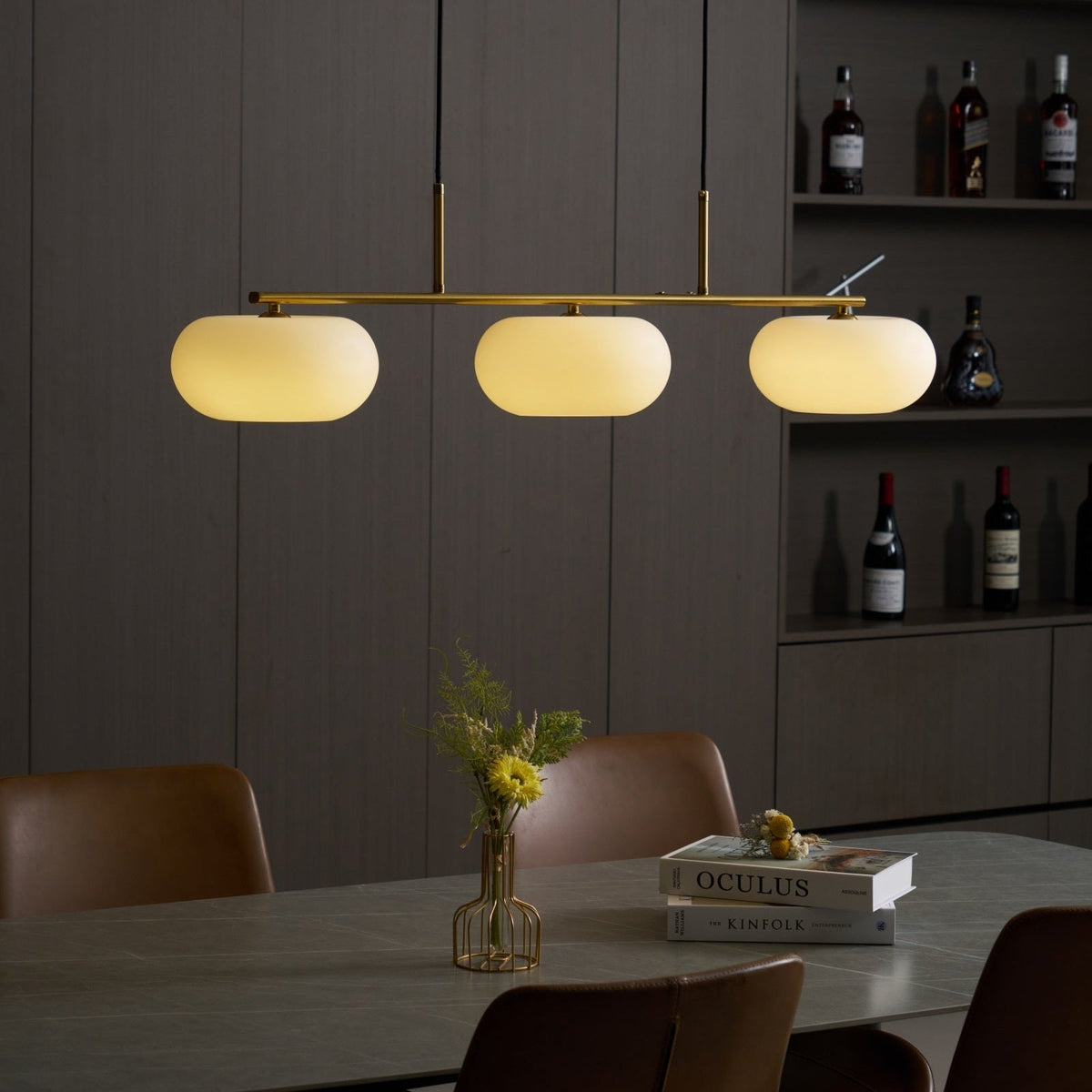Lámpara colgante lineal Calima – dorada encendida sobre una mesa de comedor