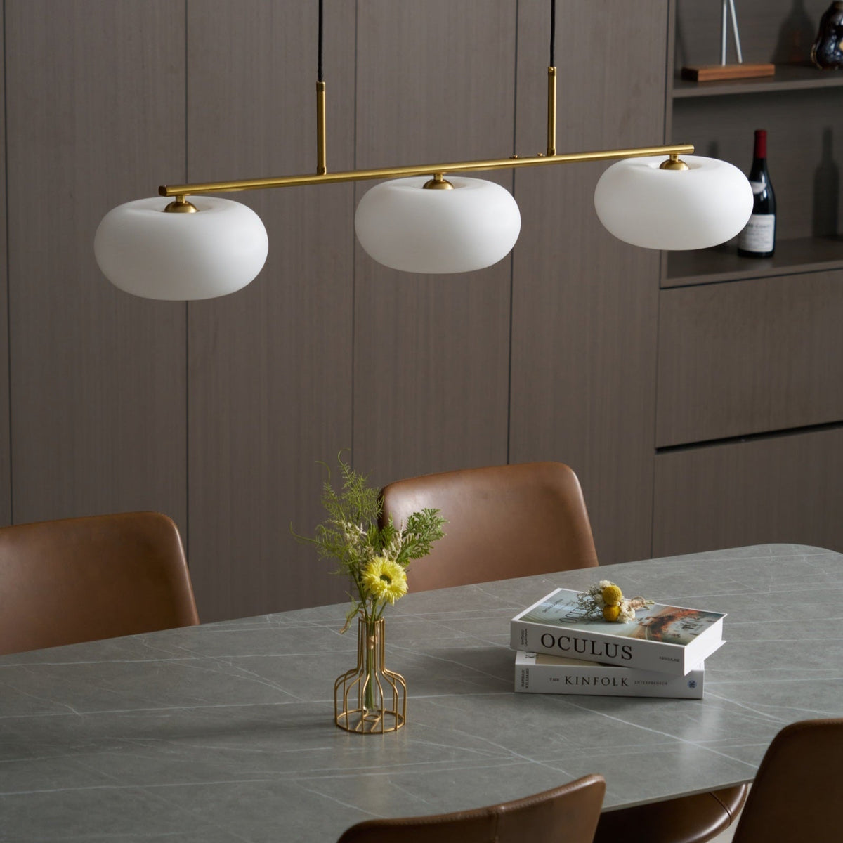 Lámpara colgante lineal Calima – dorada apagada sobre una mesa de comedor