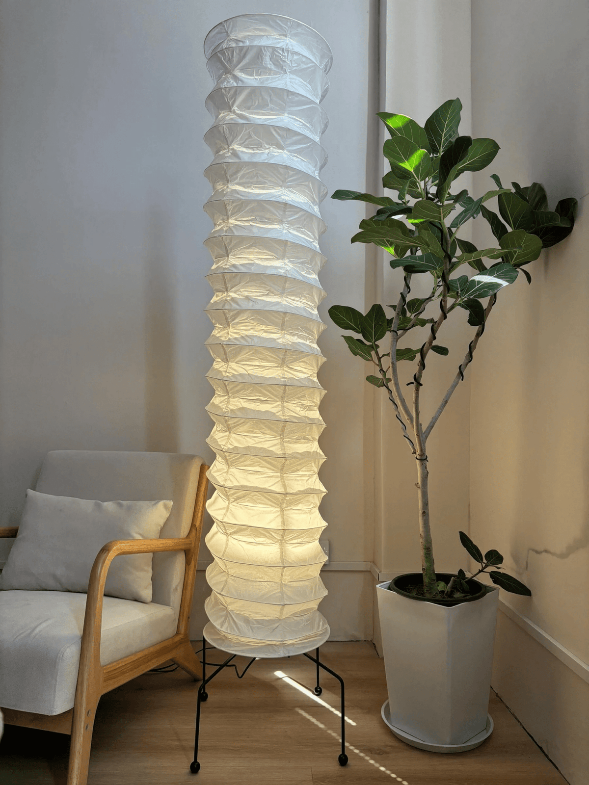 Lámpara de pie columna de papel de arroz Kiluma – encendida junto a una planta