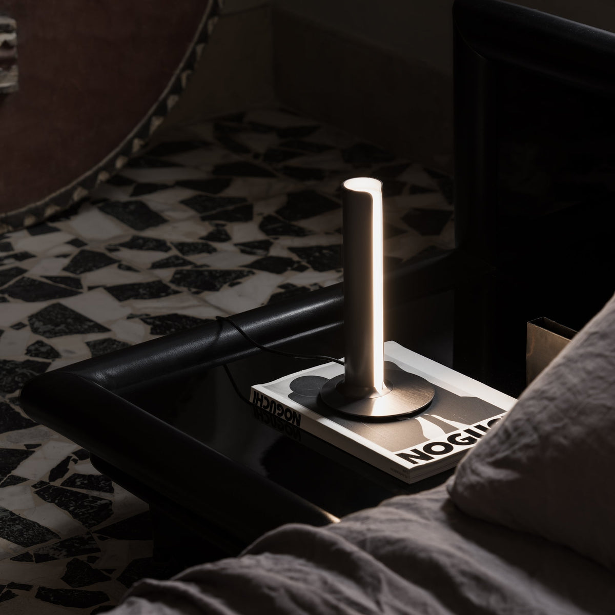 Lámpara de mesa LED cilíndrica Ostela – encendida sobre una mesita de noche