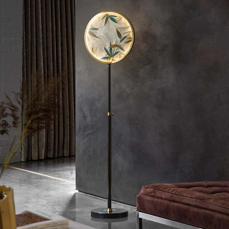 Lámpara de pie con disco de vidrio Zenavi – encendida junto a un sillón granate