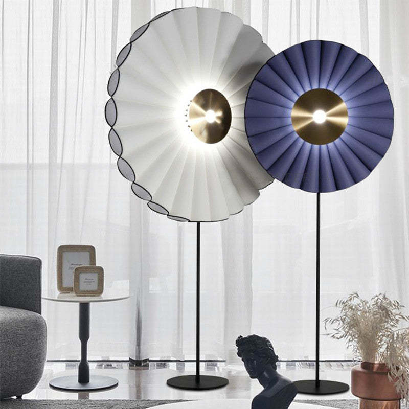 Lámpara de pie LED con disco plisado Zirena – blanca y azul junto a una ventana