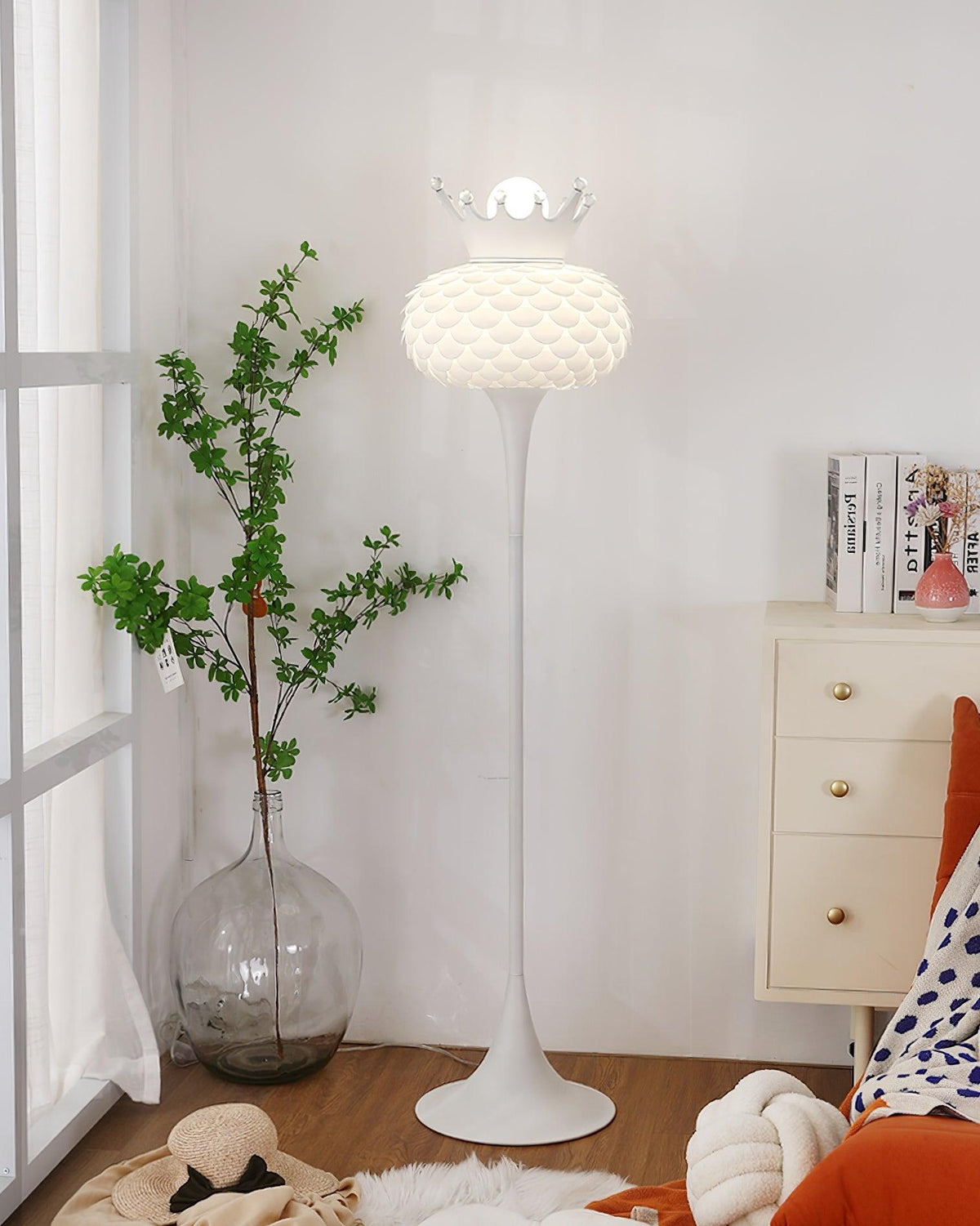 Lámpara de pie blanca con corona y pantalla texturizada Halvira – junto a una cómoda blanca y una planta