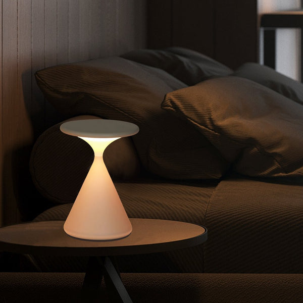 Lámpara de mesa recargable Relina – en blanco junto a un sofá en penumbra