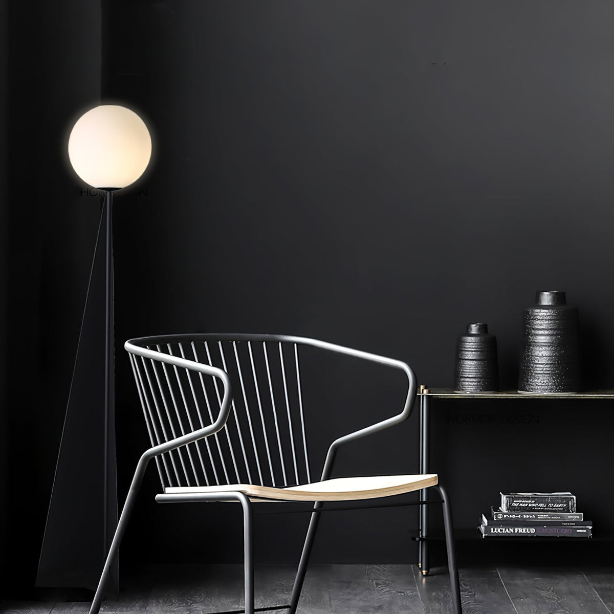 Lámpara de pie con esfera blanca y base triangular negra Pelia – en un rincón oscuro con una silla de alambre