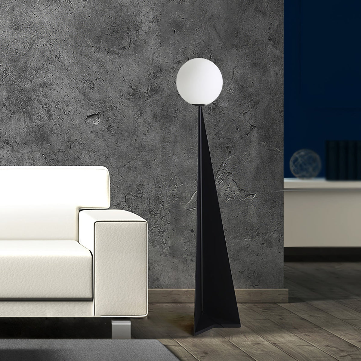 Lámpara de pie con esfera blanca y base triangular negra Pelia – junto a un sofá blanco y una pared de cemento