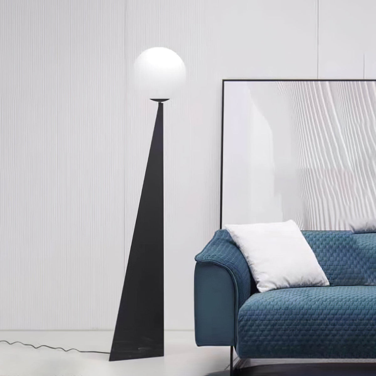 Lámpara de pie con esfera blanca y base triangular negra Pelia – junto a un sofá azul