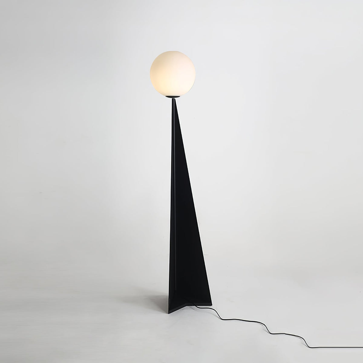 Lámpara de pie con esfera blanca y base triangular negra Pelia – encendida sobre fondo gris claro