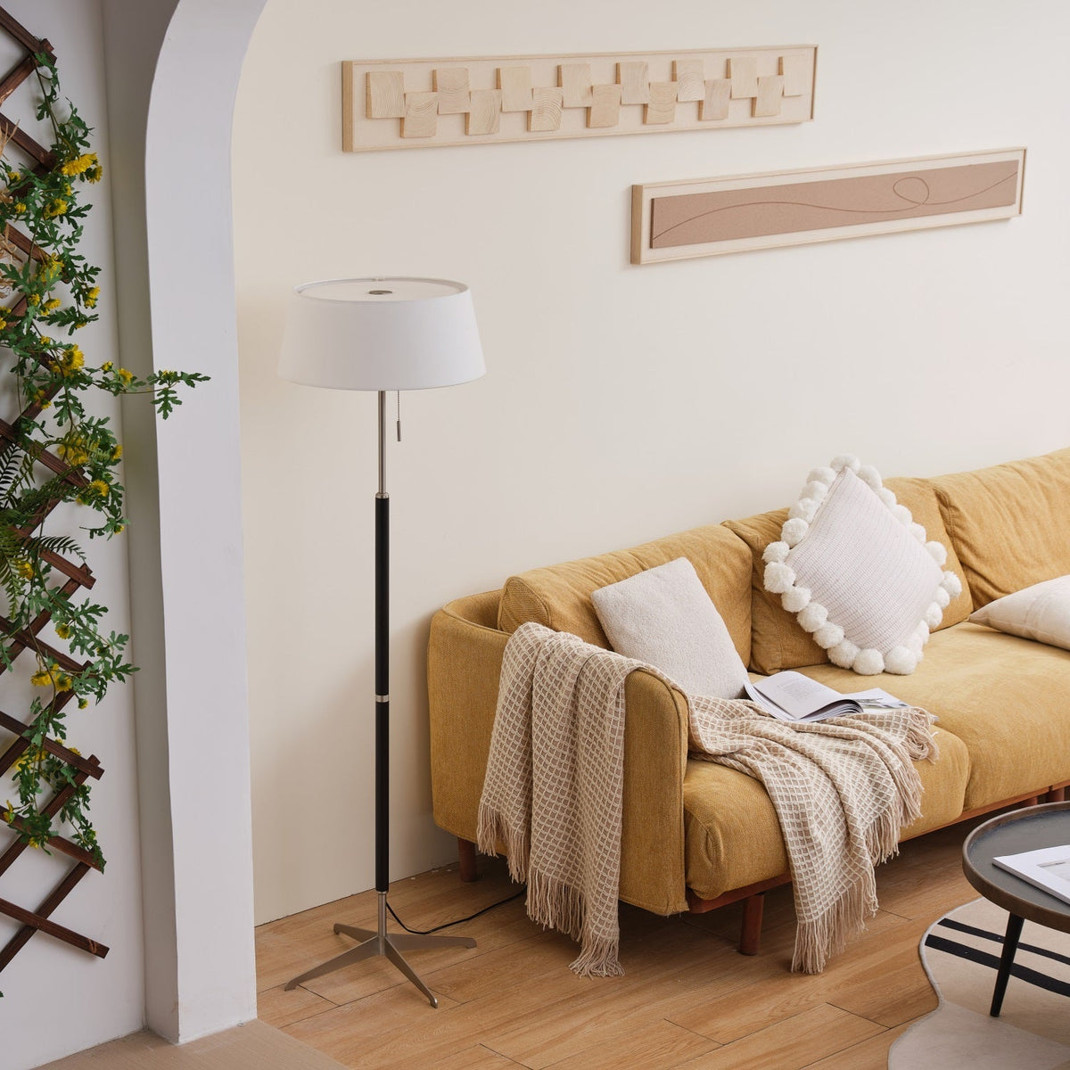 Lámpara de pie con base trípode y pantalla de tela blanca Iluma – apagada junto a un sofá