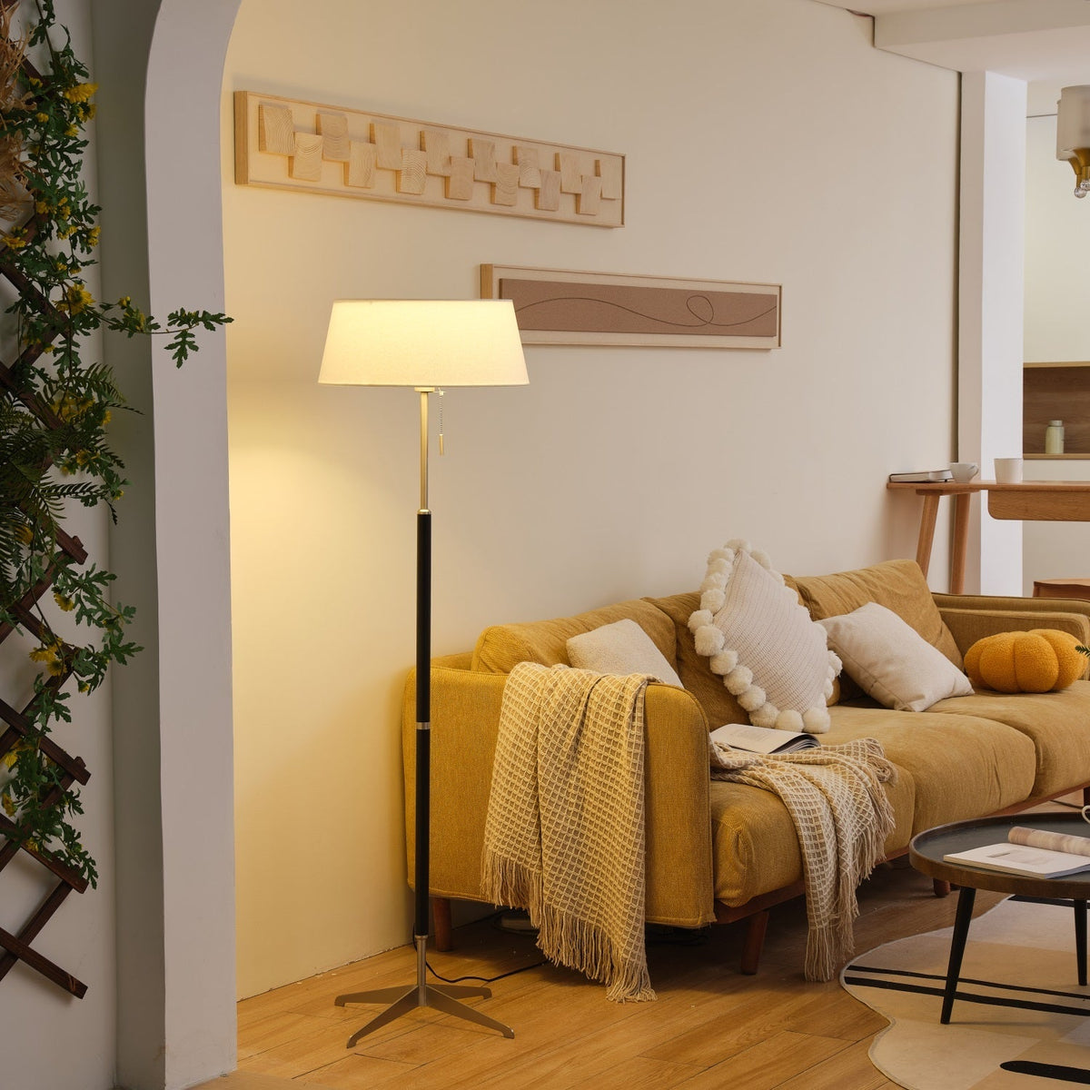 Lámpara de pie con base trípode y pantalla de tela blanca Iluma – encendida en un salón con arco
