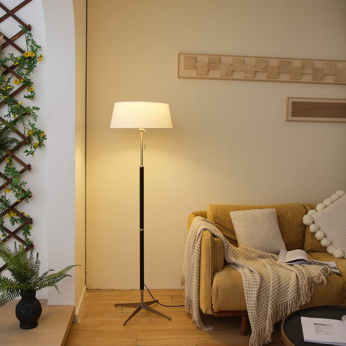 Lámpara de pie con base trípode y pantalla de tela blanca Iluma – encendida junto a una planta
