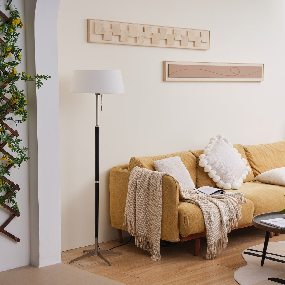 Lámpara de pie con base trípode y pantalla de tela blanca Iluma – apagada junto a un sofá