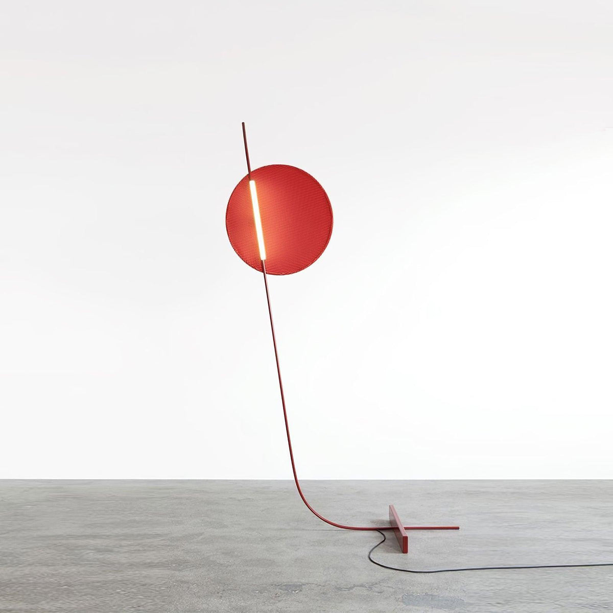 Lámpara de pie LED roja con disco de luz y varilla curva Oriola – sobre suelo de cemento pulido