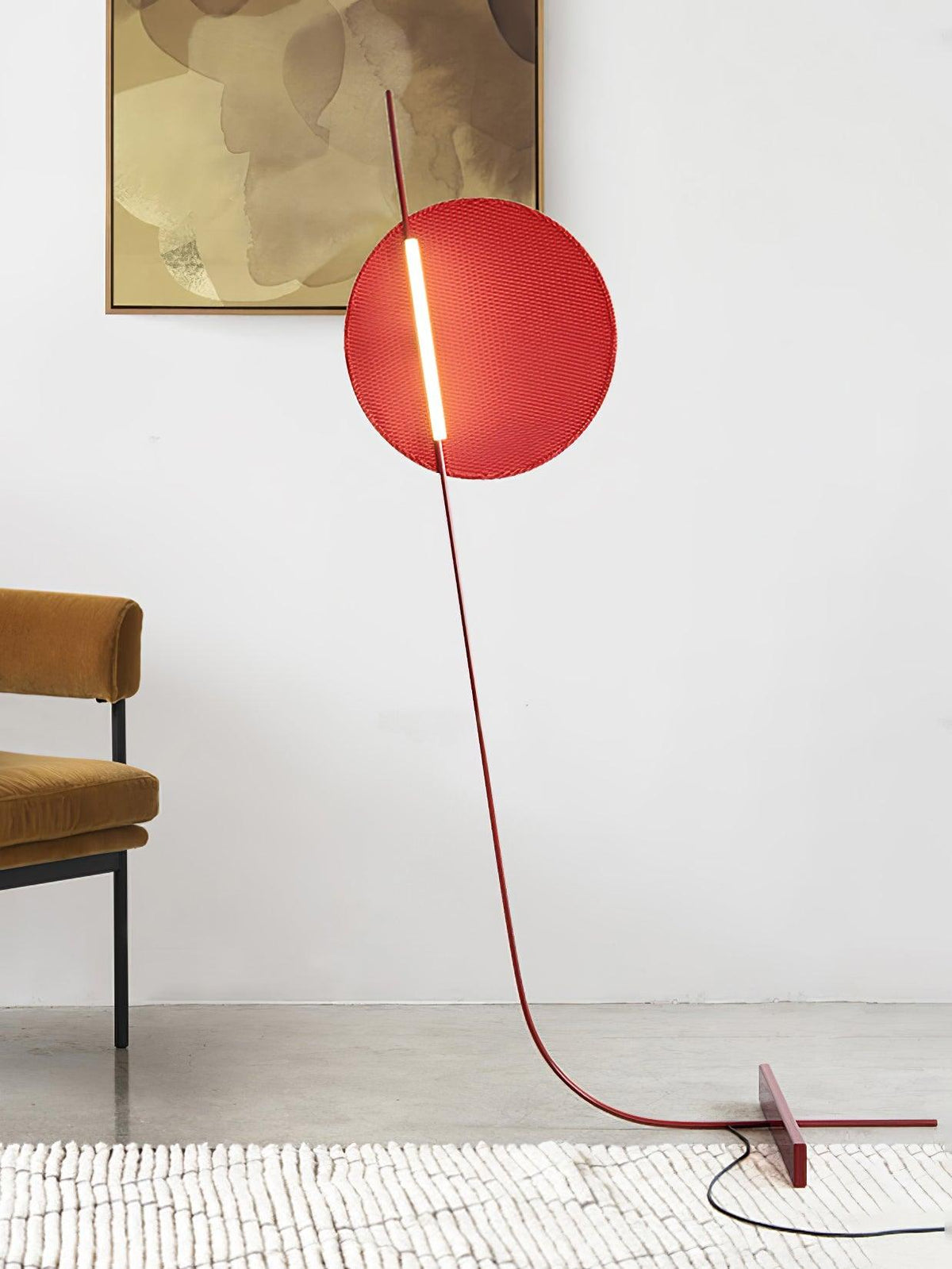 Lámpara de pie LED roja con disco de luz y varilla curva Oriola – junto a una butaca ocre