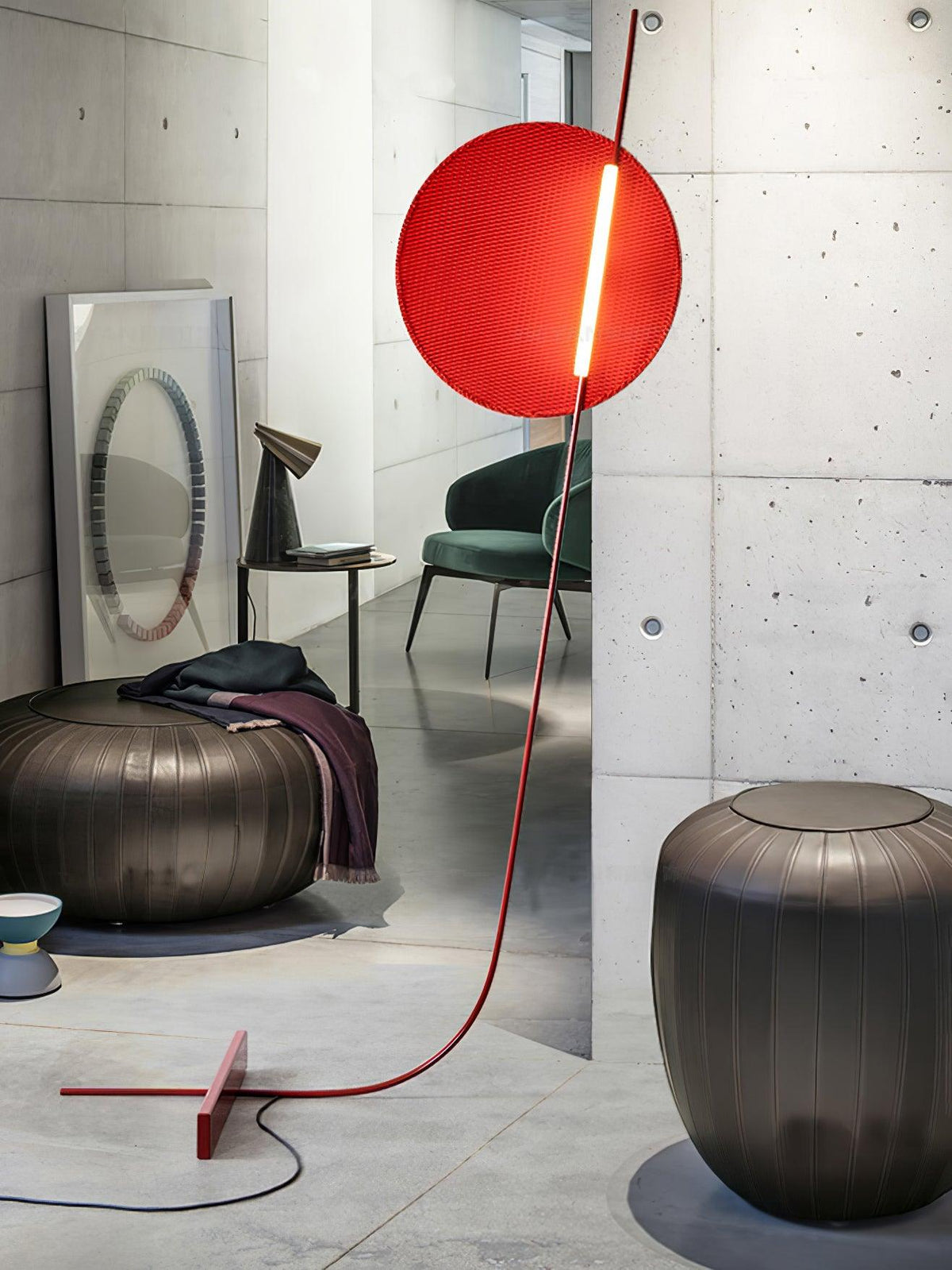 Lámpara de pie LED roja con disco de luz y varilla curva Oriola – junto a un puf de cemento