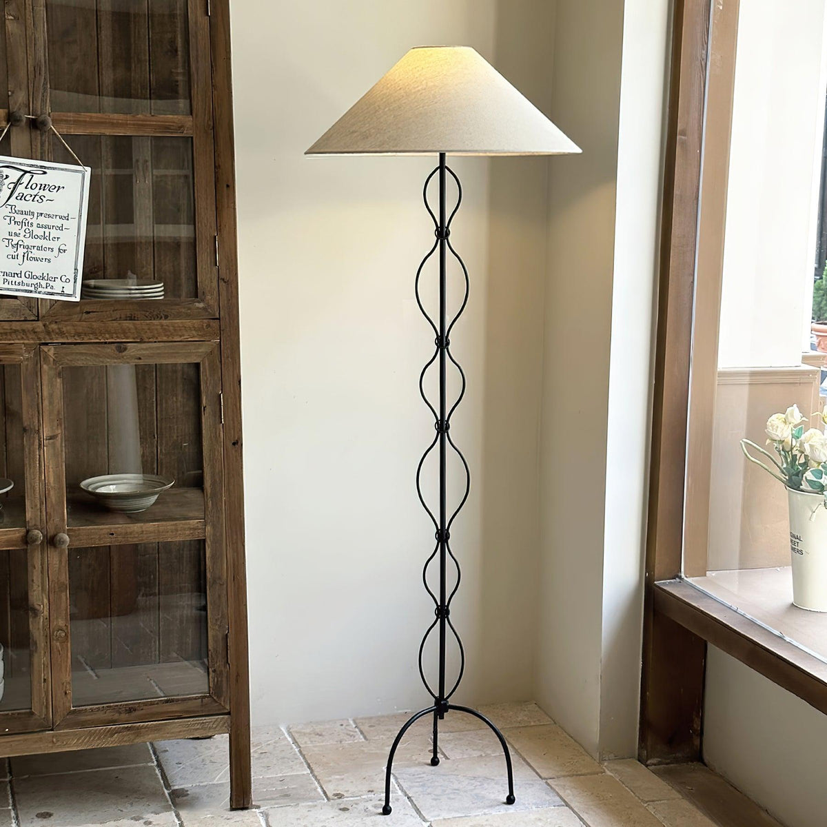 Lámpara de pie de hierro forjado Rizalia – junto a una vitrina de madera