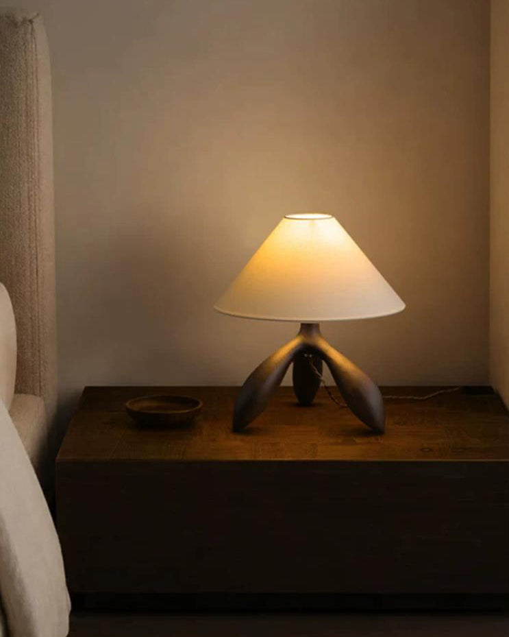Lámpara de mesa trípode Simela – encendida en una mesita oscura