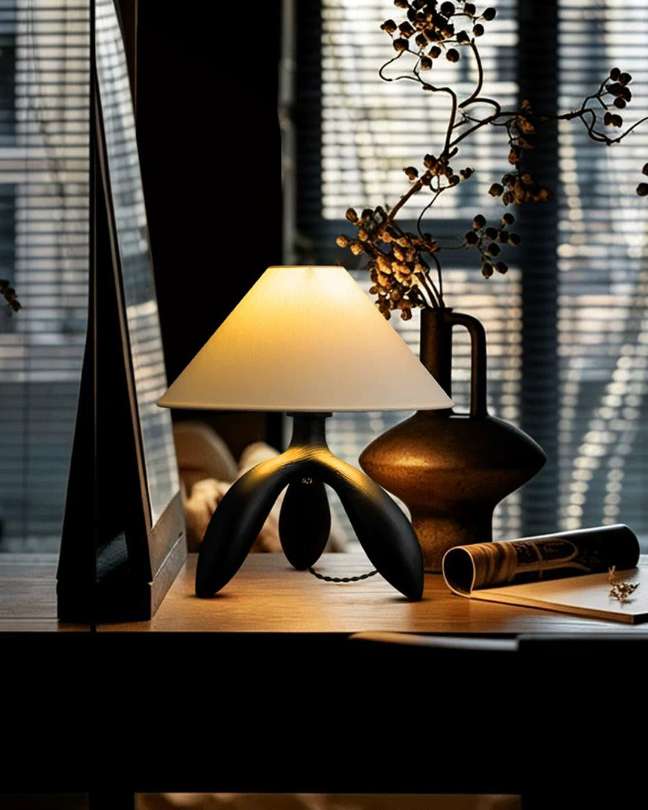 Lámpara de mesa trípode Simela – negro encendida sobre un escritorio