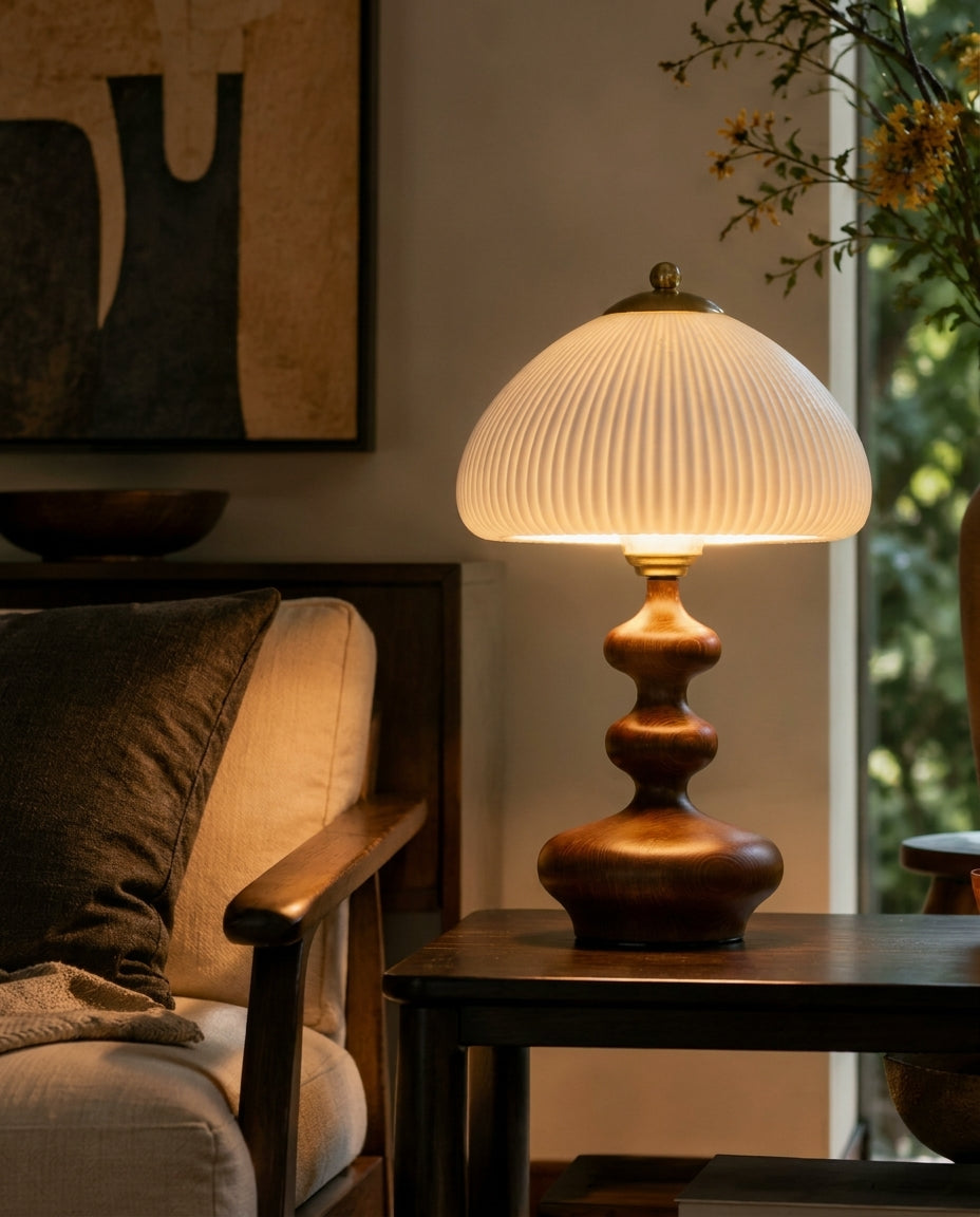 Lámpara de mesa de madera torneada Ruecola – encendida en nogal junto a una butaca