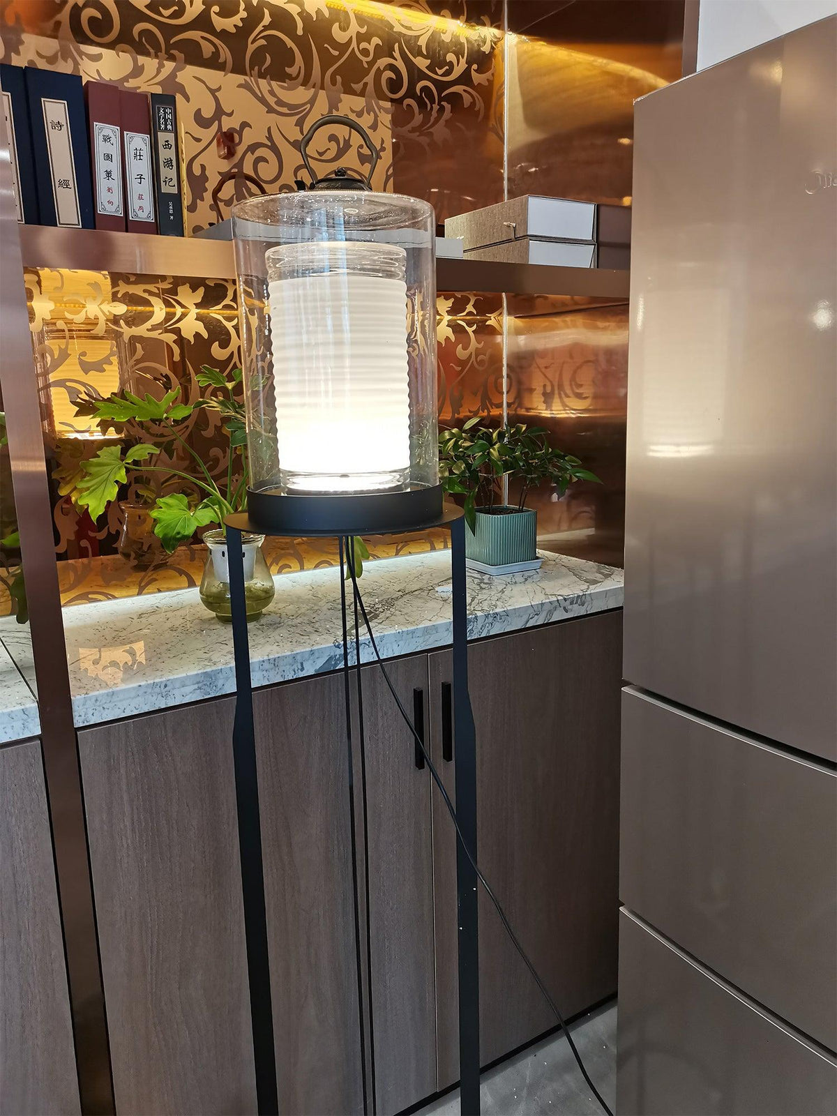 Lámpara de pie LED de doble cilindro de vidrio y estructura negra Navira – en una estantería junto a un frigorífico