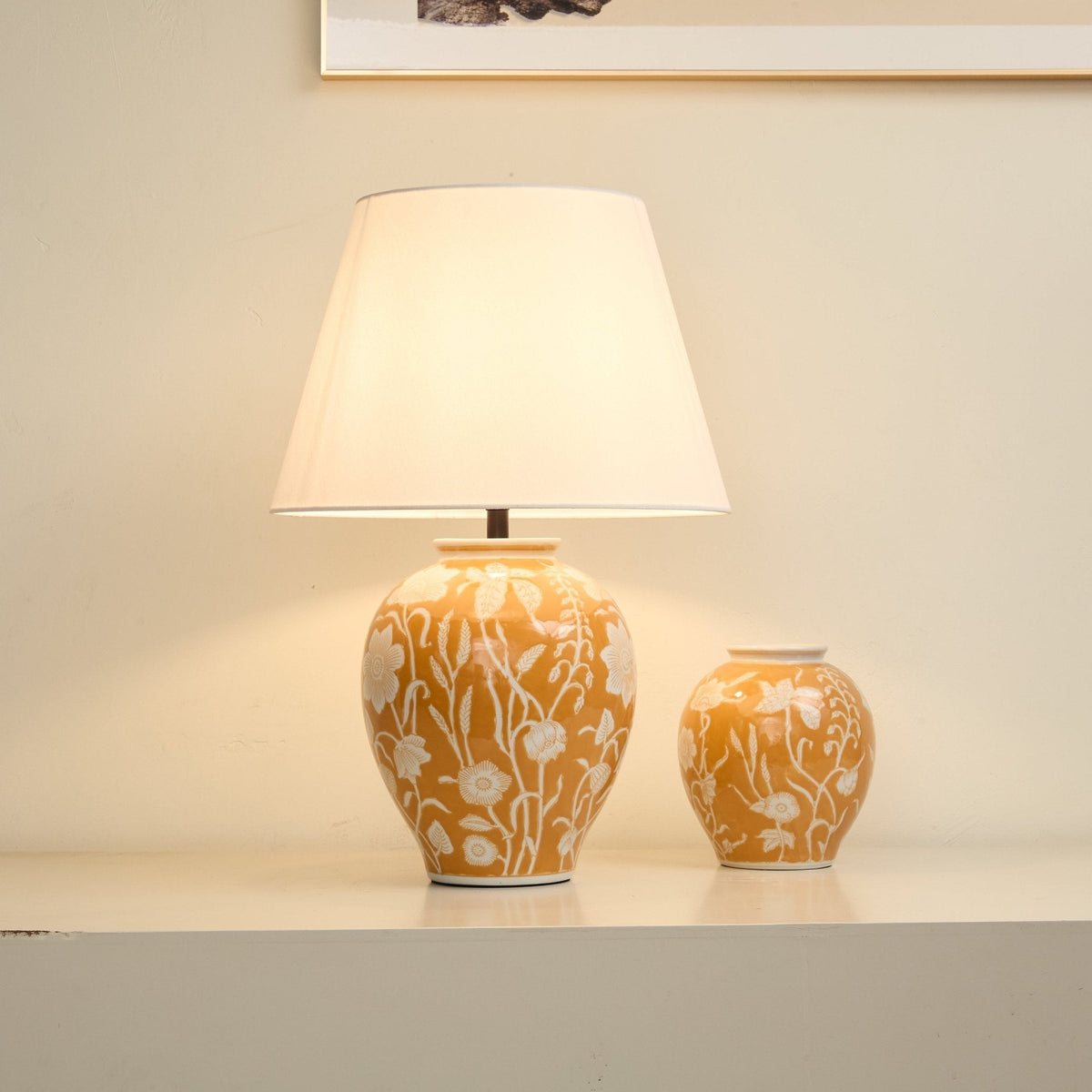 Lámpara de mesa de cerámica floral Vayelia – encendida sobre una repisa con un jarrón a juego