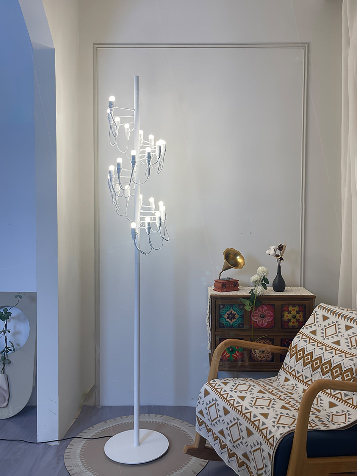 Lámpara de pie escultórica con múltiples bombillas en espiral Norelia – blanca junto a un sillón estampado