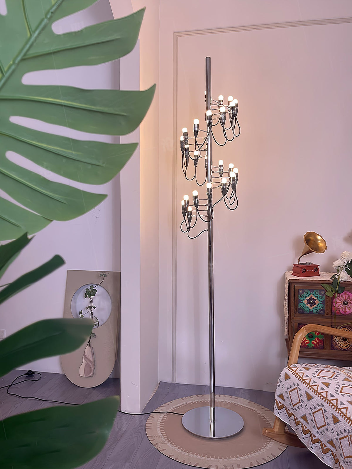 Lámpara de pie escultórica con múltiples bombillas en espiral Norelia – blanca en un rincón con planta y sillón estampado