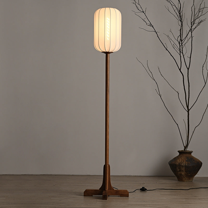 Lámpara de pie farol de tela Tolena – encendida junto a un jarrón con ramas