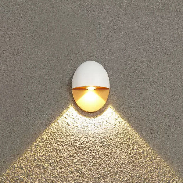 Aplique de pared exterior Yolena ovalado – blanco y dorado encendido sobre pared texturizada