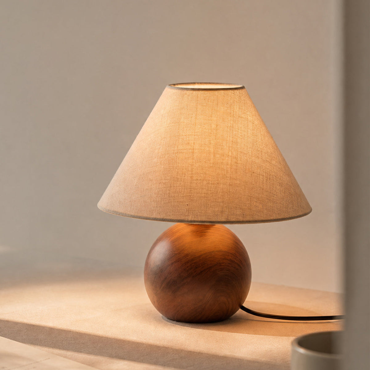 Lámpara de mesa efecto nogal Ulmara – encendida sobre una mesa de madera