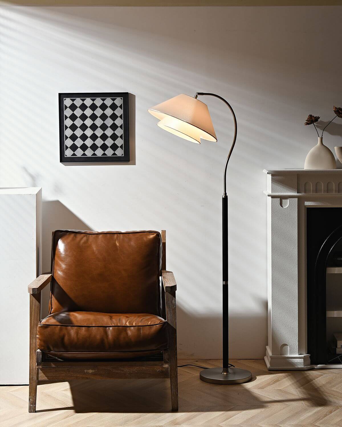 Lámpara de pie de arco Elvera – en negro junto a un sillón de cuero