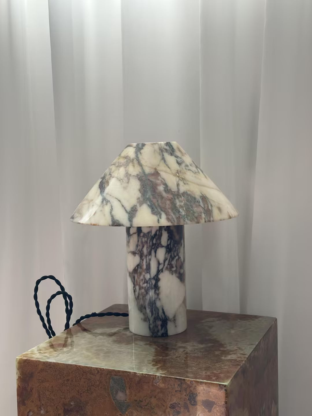 Lámpara de mesa de mármol Setona – sobre un pedestal de madera junto a cortinas