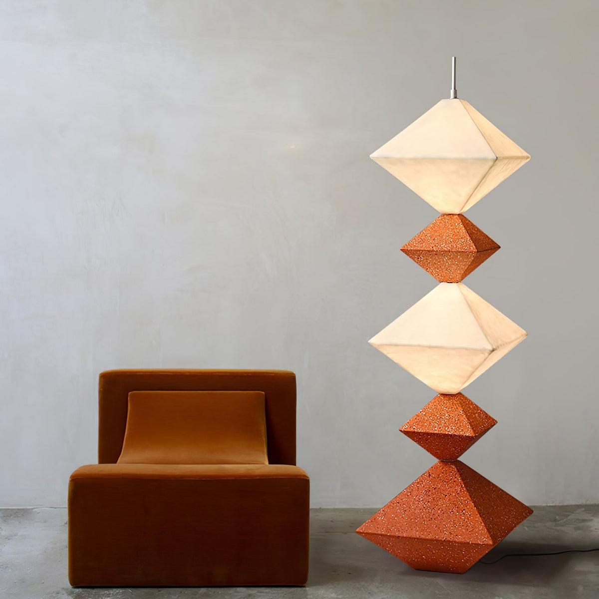 Lámpara de pie LED con rombos apilados Peluma – en naranja y blanco junto a un sillón marrón