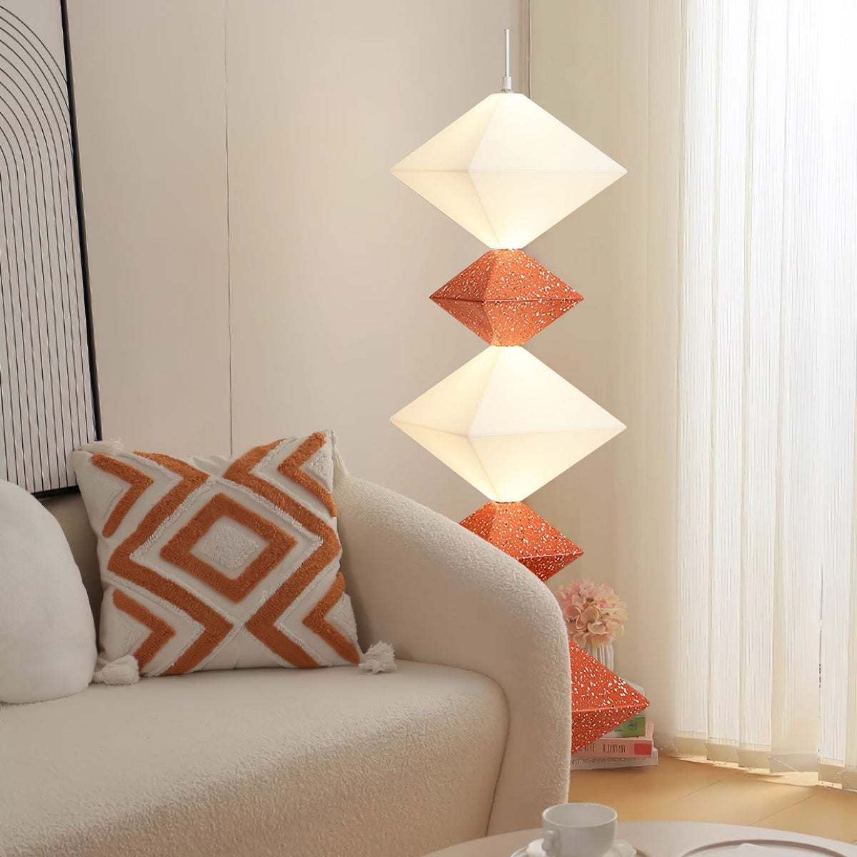 Lámpara de pie LED con rombos apilados Peluma – en naranja y blanco junto a un sofá crema