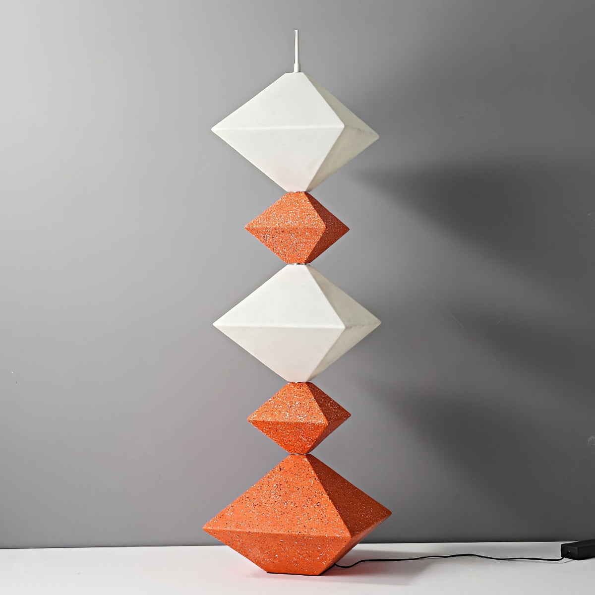 Lámpara de pie LED con rombos apilados Peluma – en naranja y blanco apagada sobre pared gris