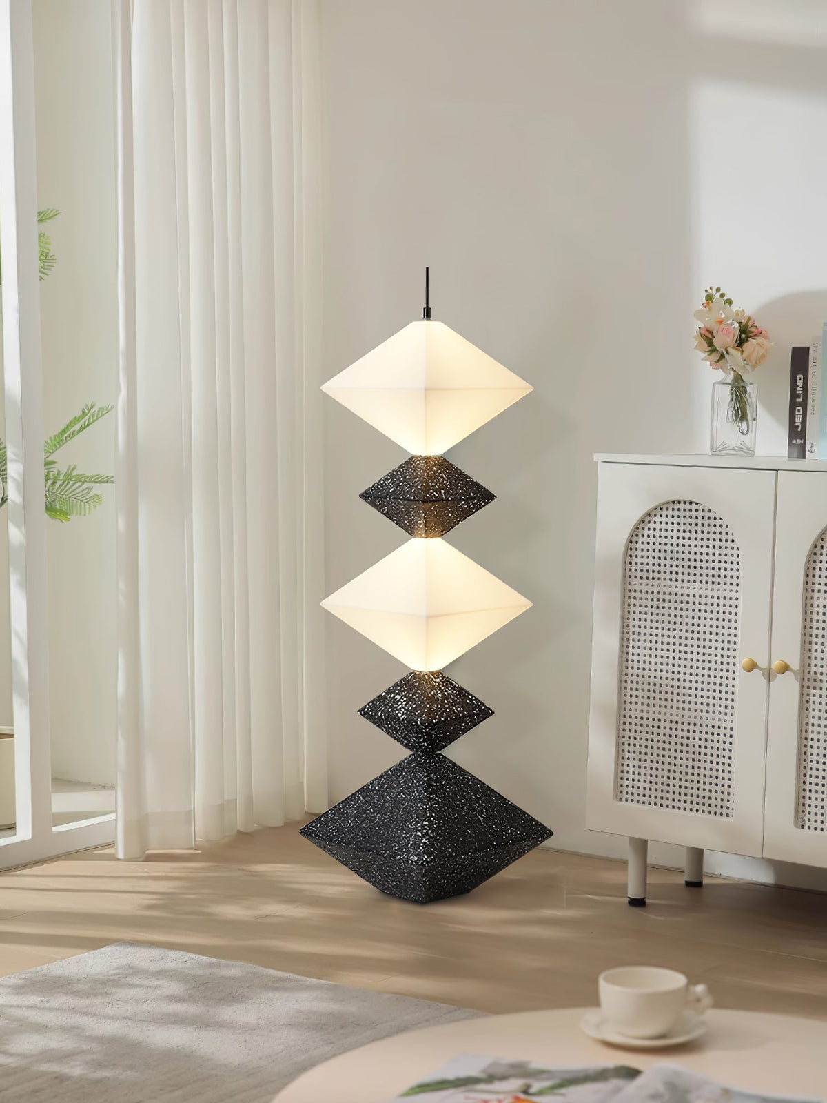 Lámpara de pie LED con rombos apilados Peluma – en negro y blanco junto a un aparador de ratán