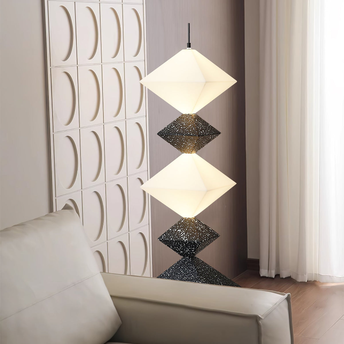Lámpara de pie LED con rombos apilados Peluma – en negro y blanco junto a un sofá y pared acanalada