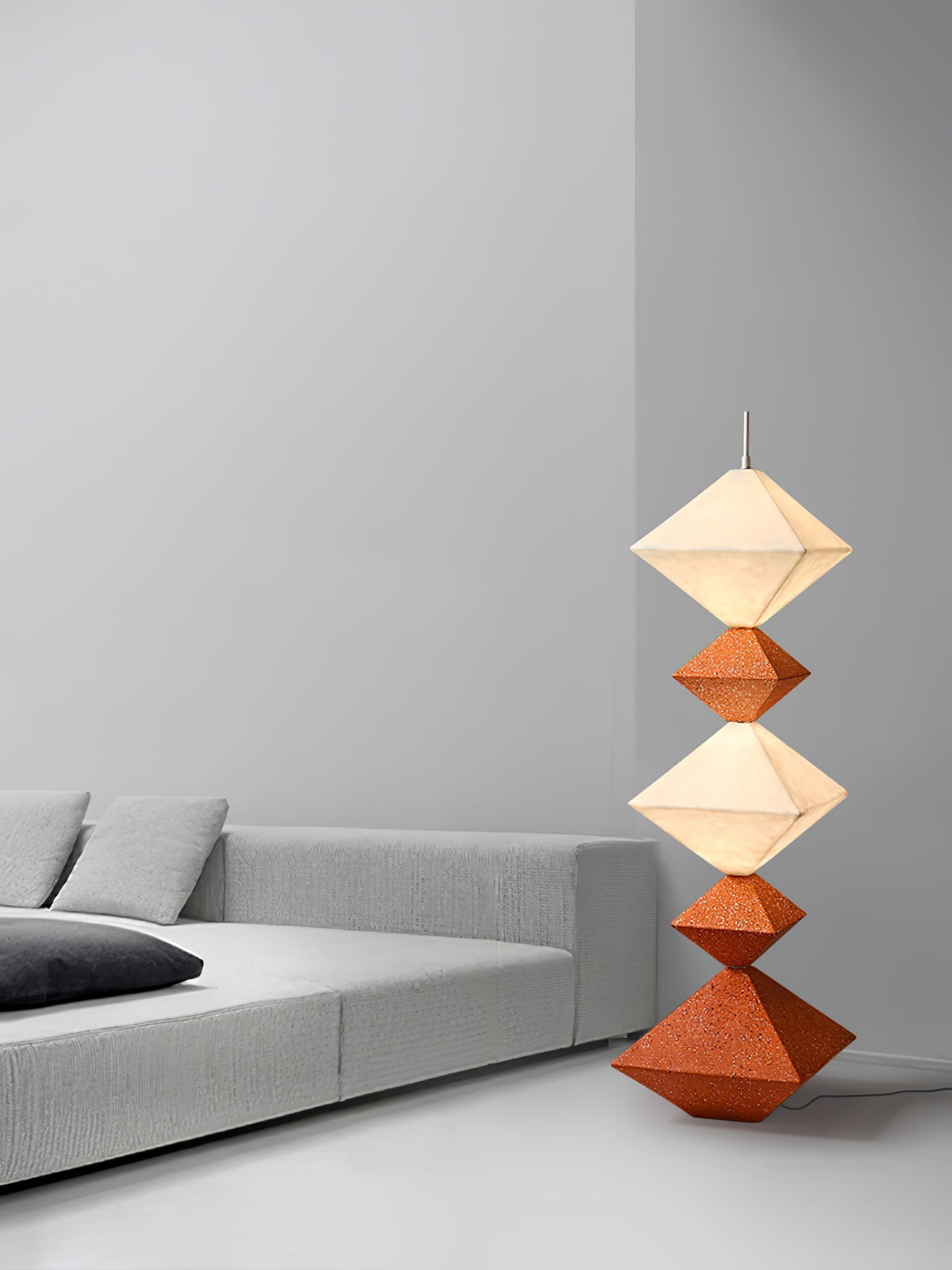 Lámpara de pie LED con rombos apilados Peluma – en naranja y blanco junto a un sofá gris