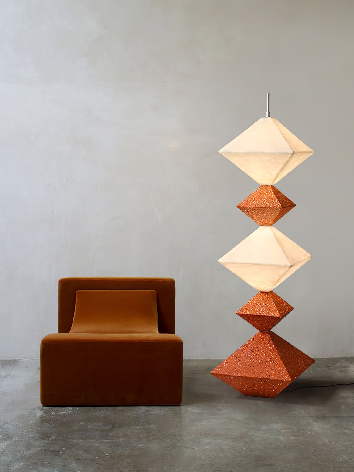 Lámpara de pie LED con rombos apilados Peluma – en naranja y blanco junto a un sillón marrón