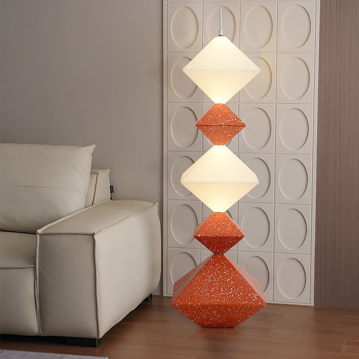 Lámpara de pie LED con rombos apilados Peluma – en naranja y blanco junto a un sofá