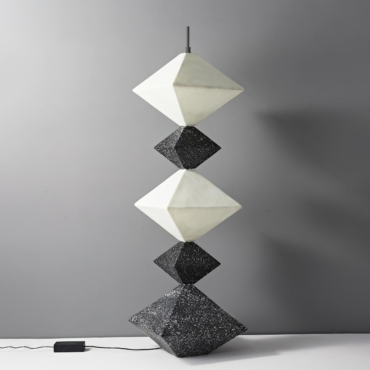 Lámpara de pie LED con rombos apilados Peluma – en negro y blanco apagada sobre pared gris