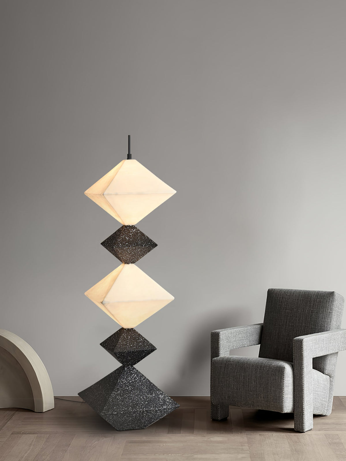 Lámpara de pie LED con rombos apilados Peluma – en negro y blanco junto a un sillón gris