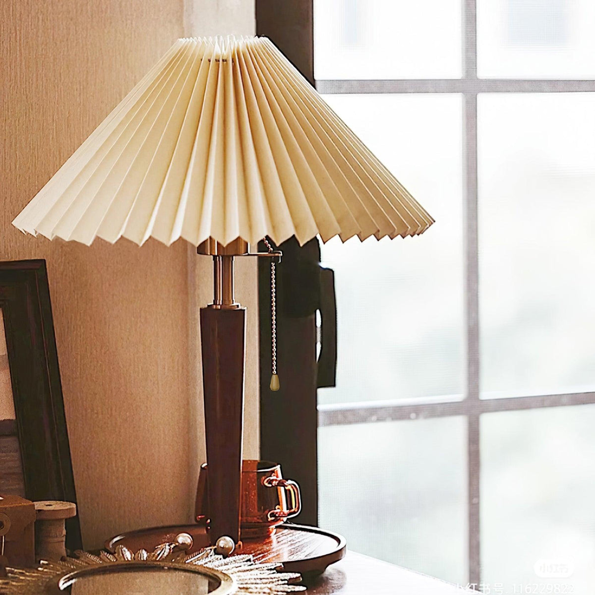 Lámpara de mesa plisada Ripela – sobre una mesita de madera